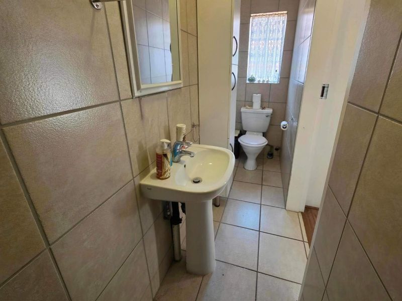A functional bathroom featuring a pedestal basin, toilet, and neutral wall and floor tiling.