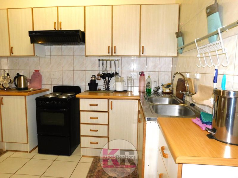 A functional kitchen featuring laminate cabinetry, laminate countertops, a stainless steel double sink, and tiled splashbacks.