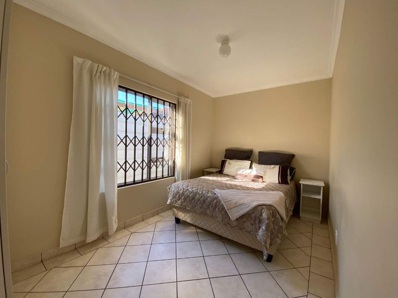 A functional bedroom featuring tiled flooring, neutral wall tones, and a window fitted with a security gate for added protection.