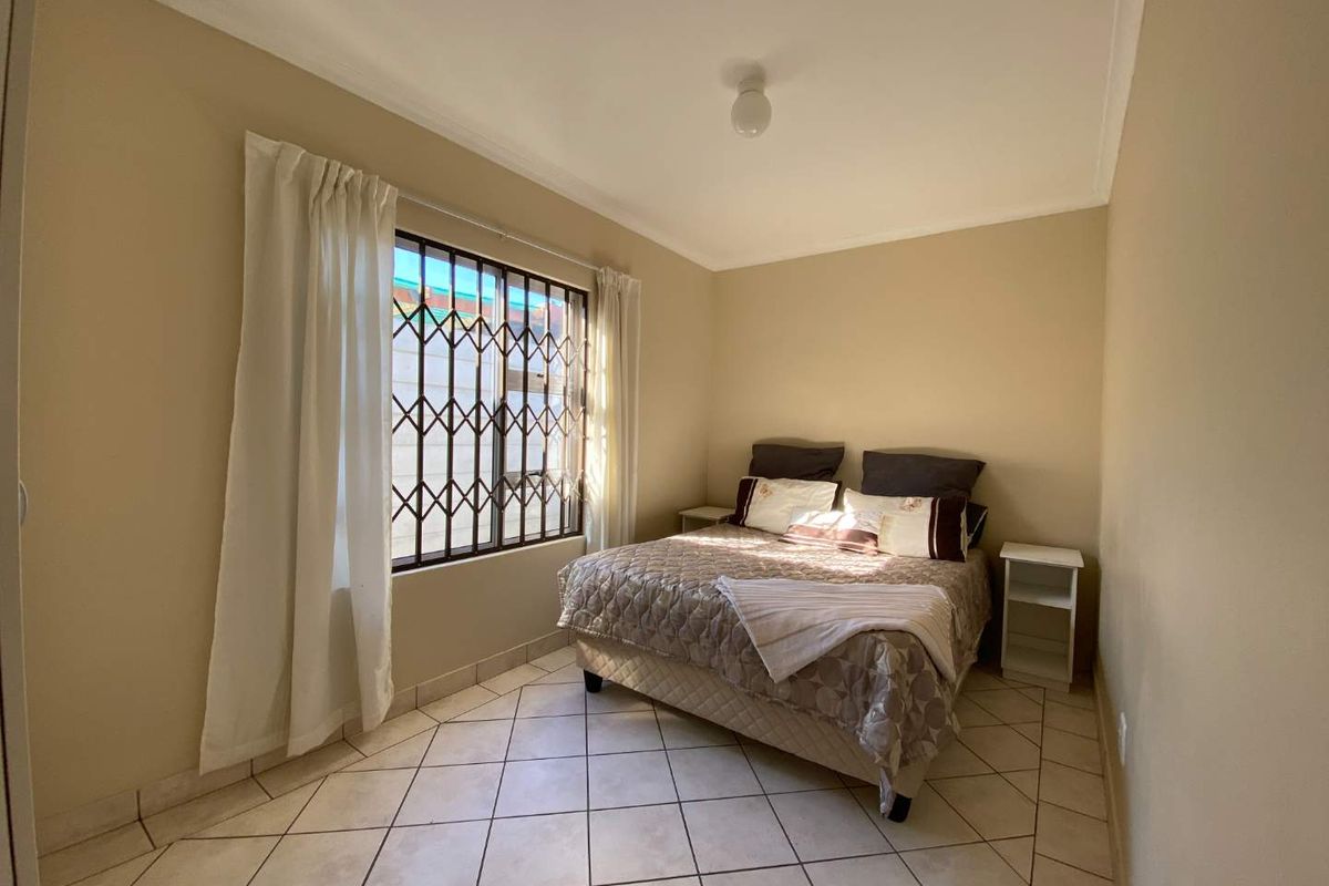 A functional bedroom featuring tiled flooring, neutral wall tones, and a window fitted with a security gate for added protection.