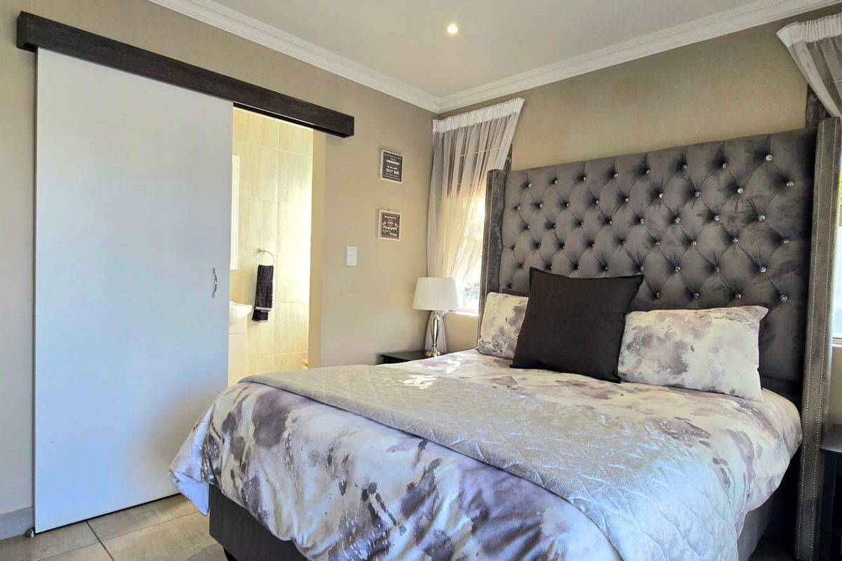 A well-maintained bedroom featuring tiled flooring, recessed downlights, and a sliding door providing access to an en-suite bathroom.