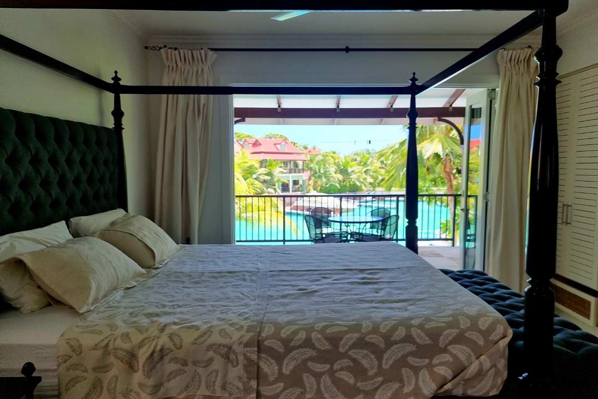 Spacious bedroom featuring a large four-poster bed and direct access to a private balcony overlooking the swimming pool area.
