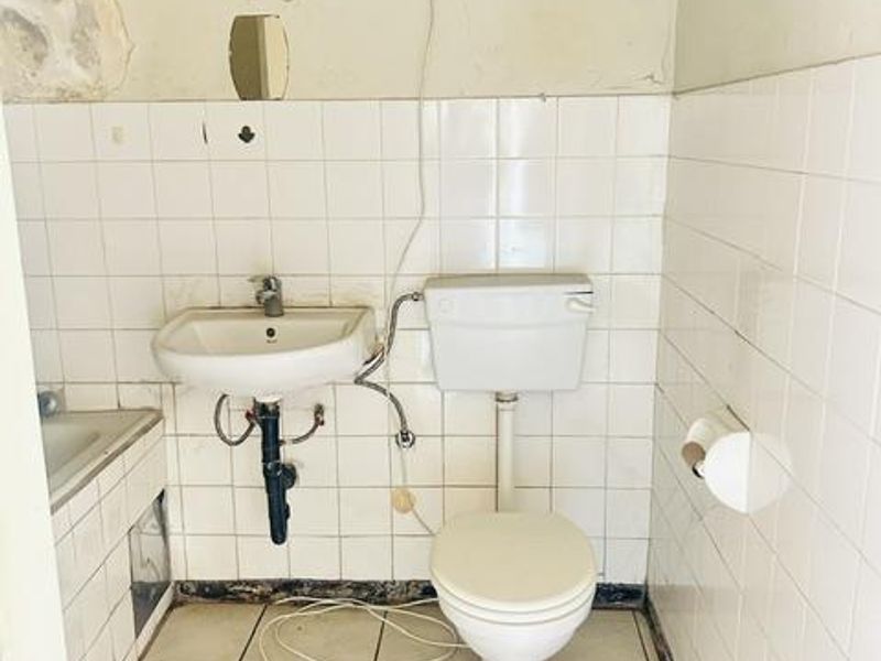 A dated bathroom featuring a wall-mounted basin and toilet, requiring significant renovation and cosmetic updates to improve its condition and functionality.