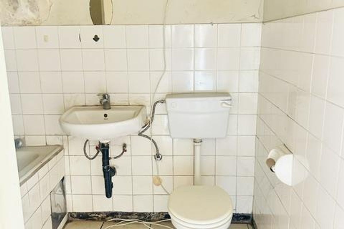 A dated bathroom featuring a wall-mounted basin and toilet, requiring significant renovation and cosmetic updates to improve its condition and functionality.