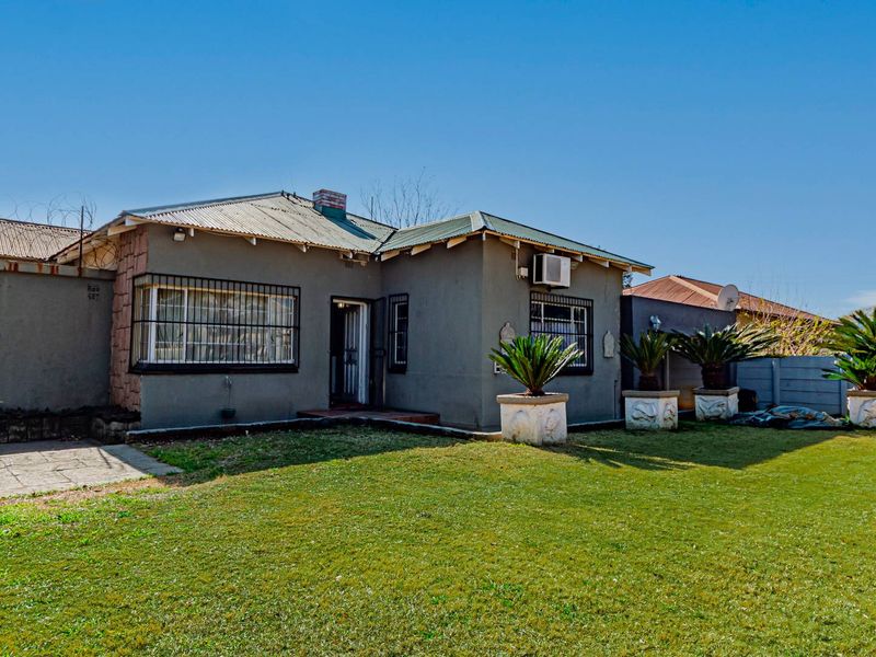 Rear view of a single-story house featuring a corrugated metal roof, security bars on windows, a paved patio, and a well-maintained lawn.