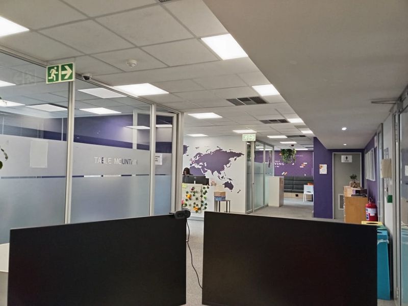 Modern office interior featuring glass-partitioned meeting rooms, suspended ceilings with recessed lighting, and a professional open-plan layout with carpeted flooring.