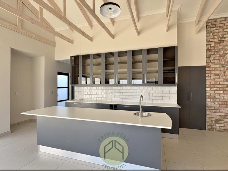 Modern kitchen featuring an island, exposed timber rafters, brick feature wall, subway tile backsplash, and ample built-in cabinetry with glass-fronted upper units.