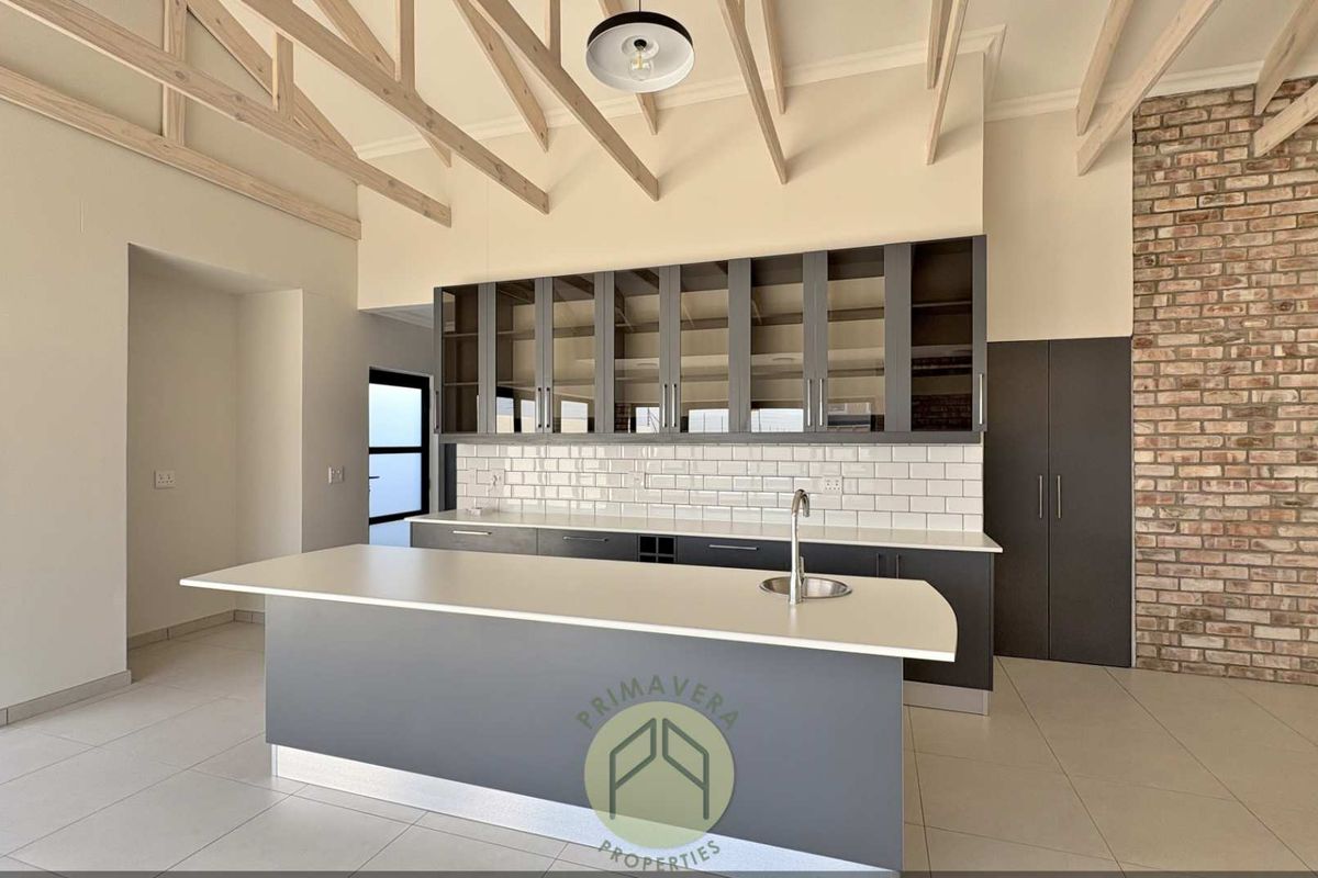 Modern kitchen featuring an island, exposed timber rafters, brick feature wall, subway tile backsplash, and ample built-in cabinetry with glass-fronted upper units.