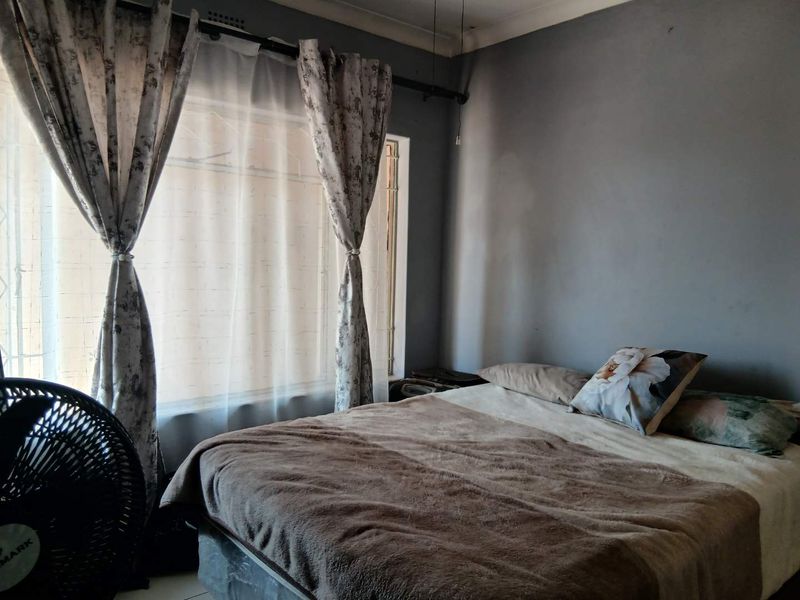 A bedroom featuring a large window with curtains and grey painted walls, providing a functional space for rest.