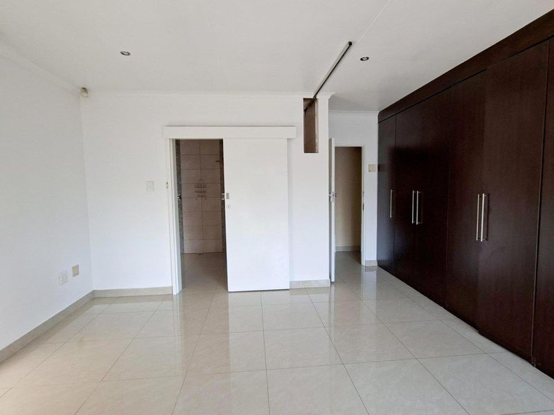 Spacious bedroom featuring large dark wood built-in cupboards, neutral tiled flooring, and an integrated air conditioning unit.