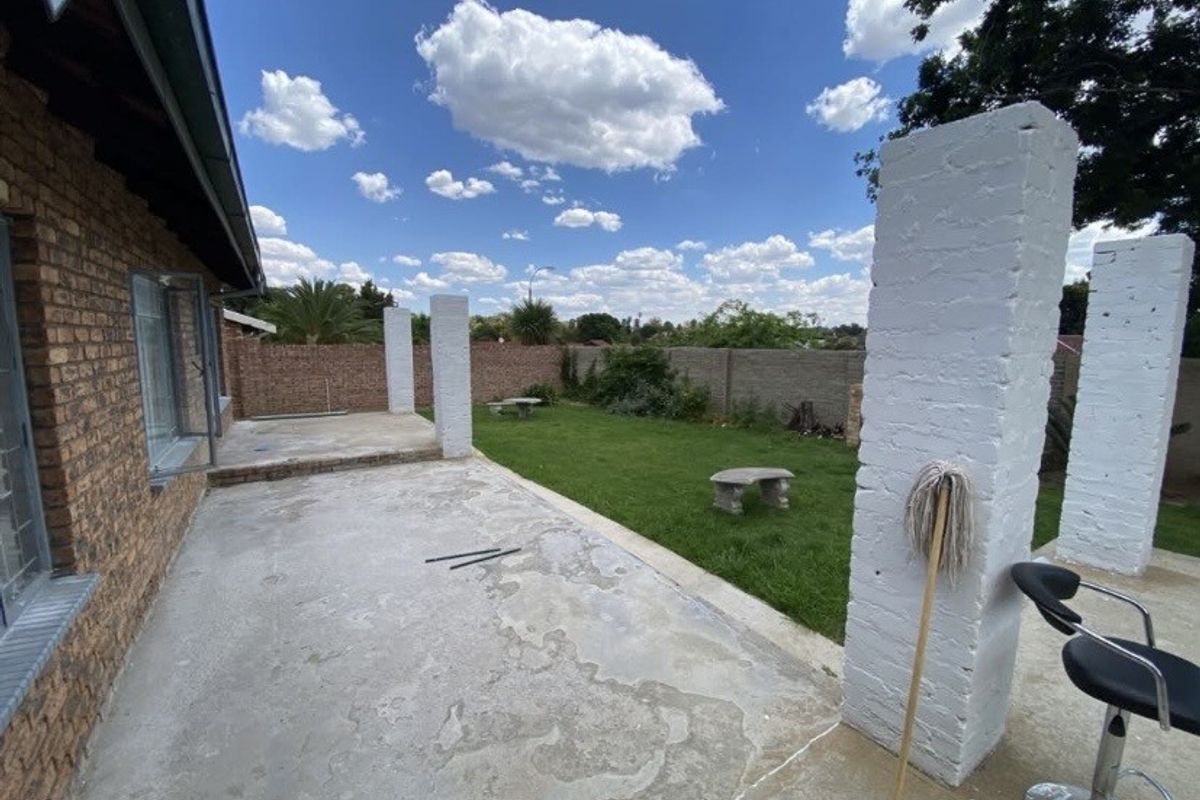 An outdoor patio area featuring concrete flooring and painted brick columns, overlooking a private garden with a perimeter brick wall.