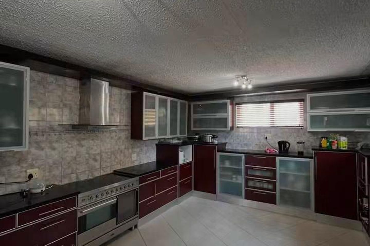 Spacious kitchen featuring dark cabinetry, stainless steel appliances, tiled backsplash, and neutral floor tiles with ample storage and counter space.