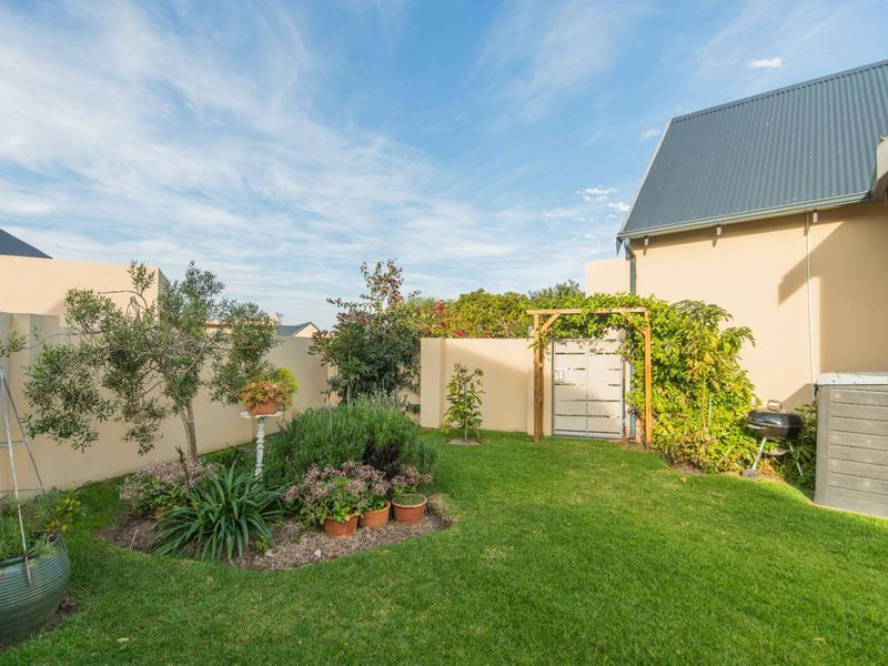 A well-maintained rear garden featuring a manicured lawn, perimeter boundary walls, a garden gate with a timber pergola, and established landscaping.