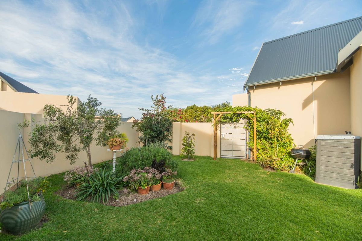 A well-maintained rear garden featuring a manicured lawn, perimeter boundary walls, a garden gate with a timber pergola, and established landscaping.