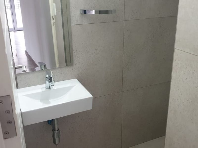 A compact, modern guest bathroom featuring a wall-mounted basin, chrome fixtures, and neutral wall tiling.