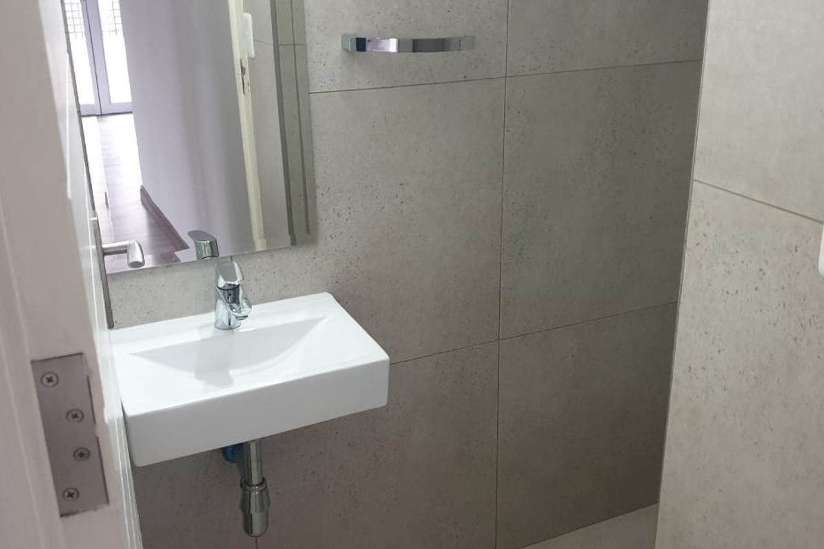 A compact, modern guest bathroom featuring a wall-mounted basin, chrome fixtures, and neutral wall tiling.