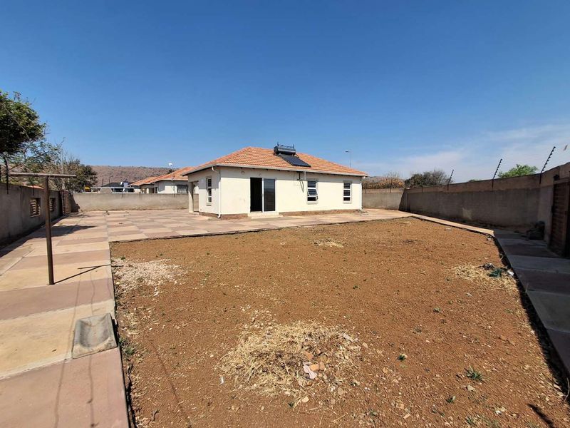 Rear view of the house featuring a tiled roof, solar water heater, paved patio area, and a large unlandscaped garden space.