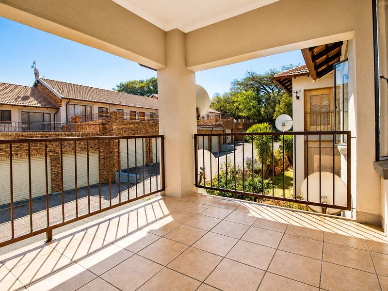 A spacious covered balcony featuring tiled flooring and a metal balustrade, offering an elevated view of the townhouse complex and surrounding area.