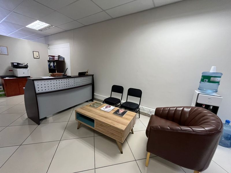 A functional office reception area featuring tiled flooring, a built-in reception desk, and a suspended ceiling with recessed lighting.