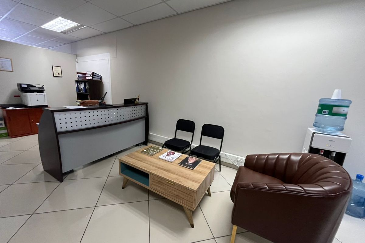 A functional office reception area featuring tiled flooring, a built-in reception desk, and a suspended ceiling with recessed lighting.