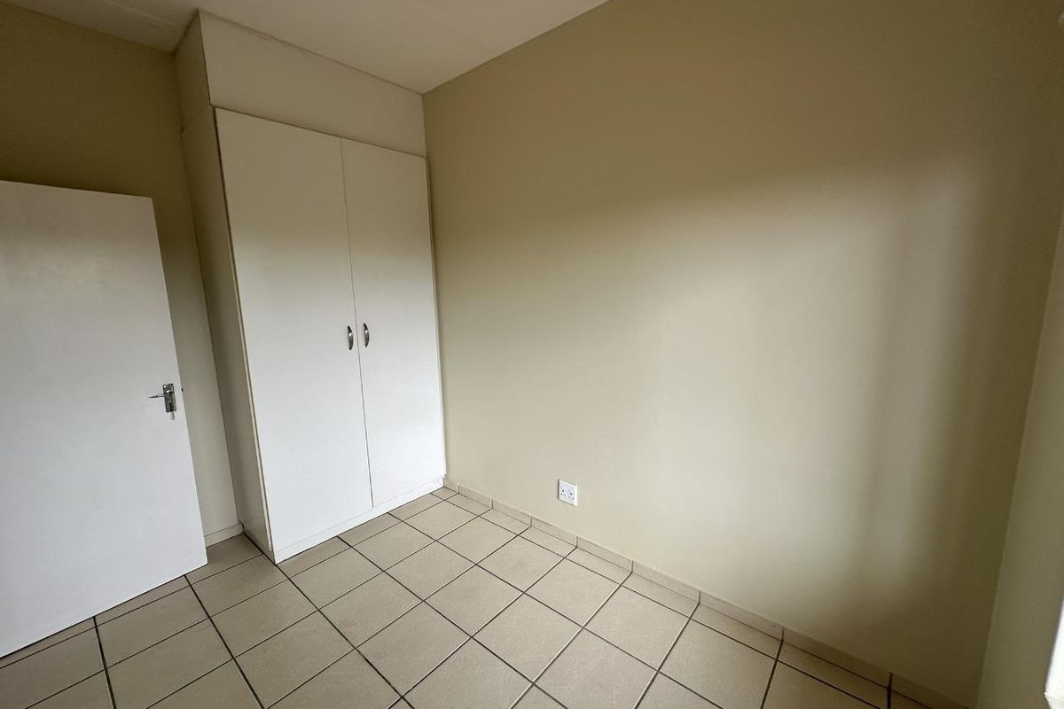 A simple, empty bedroom featuring neutral wall paint, tiled flooring, and a built-in white wardrobe.