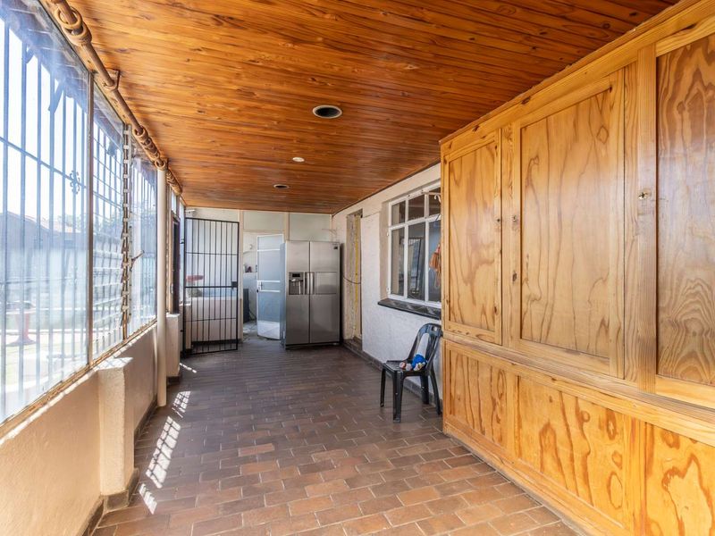 Enclosed patio area featuring a wooden ceiling, brick flooring, and extensive built-in wooden cabinetry, providing a versatile space with security bars.