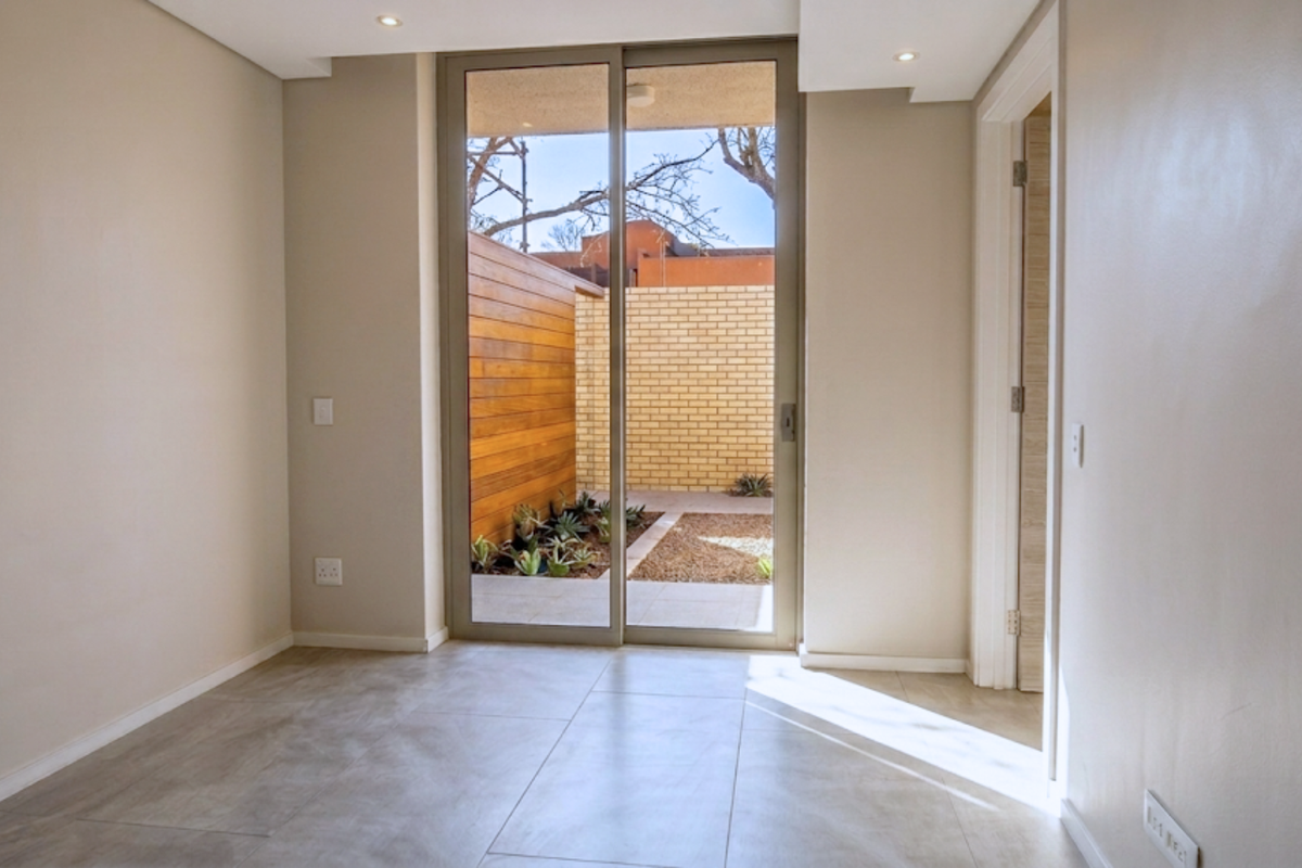 A bright, empty living area featuring large sliding glass doors that open onto a private courtyard with timber cladding and landscaped garden beds.