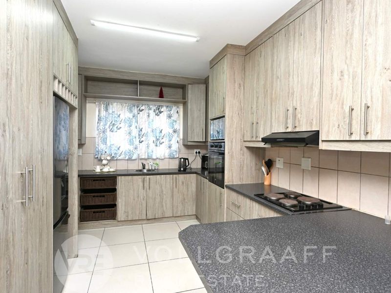 Modern kitchen featuring light wood-grain cabinetry, dark stone-look countertops, built-in oven, electric hob, and tiled flooring.