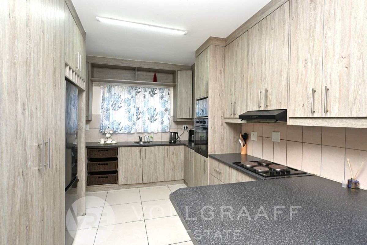 Modern kitchen featuring light wood-grain cabinetry, dark stone-look countertops, built-in oven, electric hob, and tiled flooring.