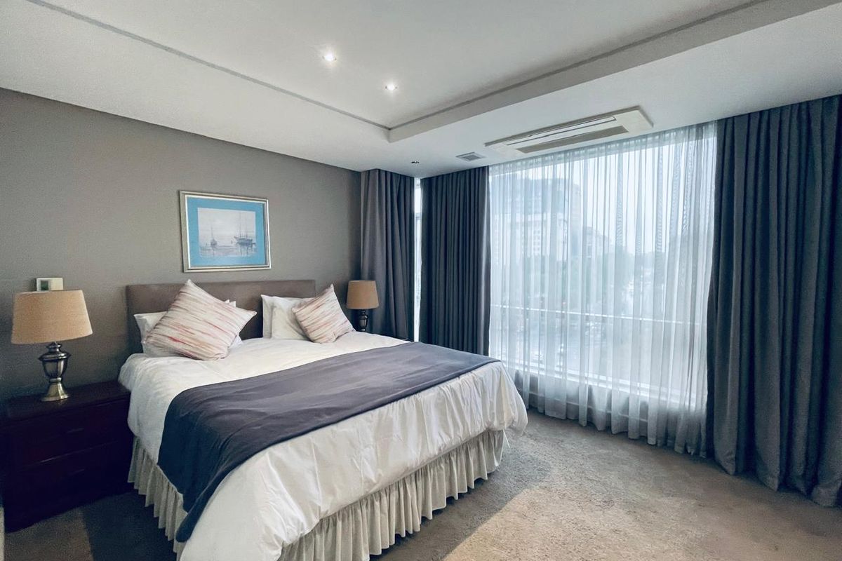 A well-maintained bedroom featuring recessed ceiling lighting, ducted air conditioning, and large floor-to-ceiling windows with elegant drapery.