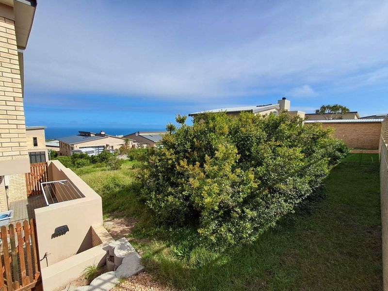 Rear exterior view of the property featuring a paved patio, lawn area, and boundary wall with distant ocean views.