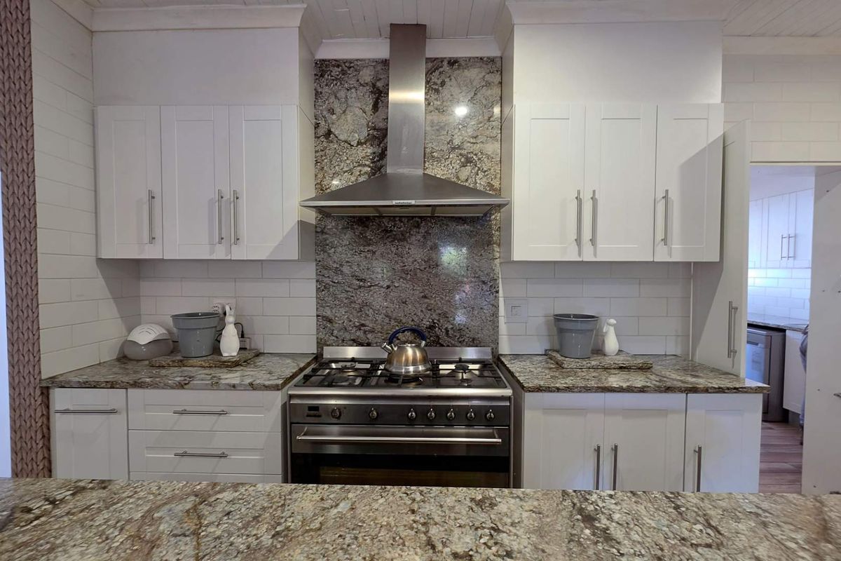 Modern kitchen featuring white shaker cabinetry, granite countertops, a subway tile backsplash, and a stainless steel gas stove with a matching extractor fan.