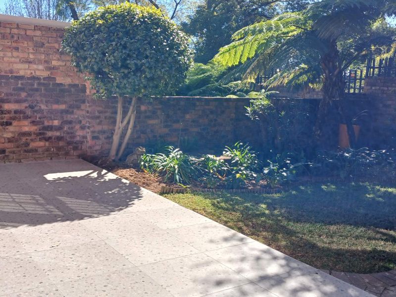 A private garden area featuring a paved patio, established garden beds, and high brick boundary walls providing a secluded outdoor space.