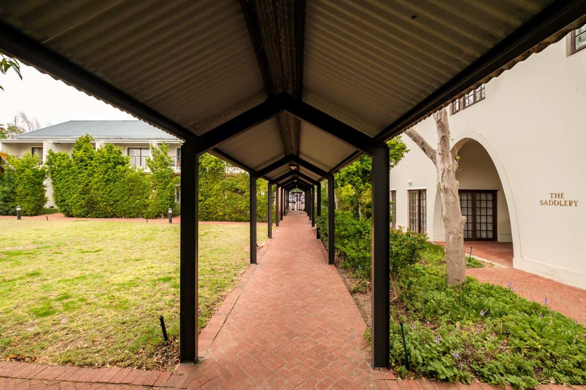 A well-maintained covered brick walkway leading through a landscaped garden area, providing sheltered access between apartment building sections.
