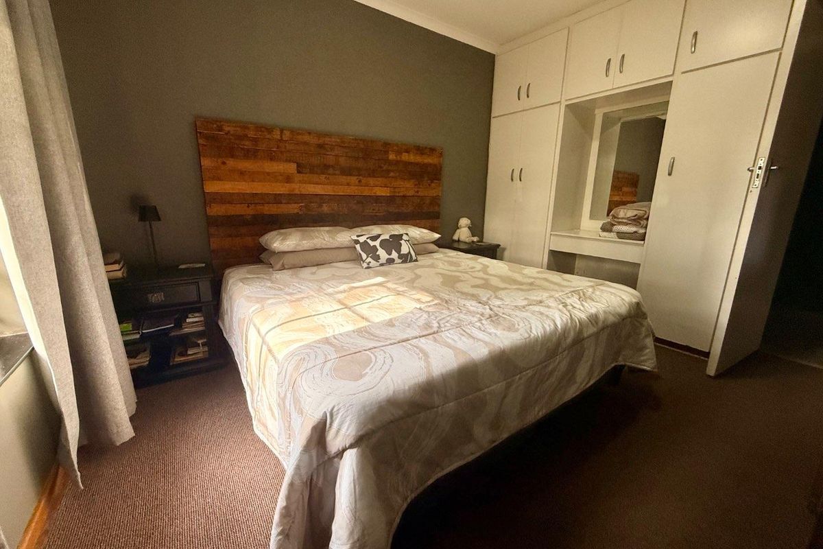 A bedroom featuring built-in floor-to-ceiling wardrobes with an integrated vanity mirror and carpeted flooring.