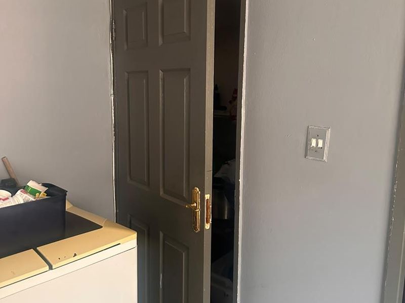 A laundry area featuring a panel door with brass hardware and tiled flooring, showing signs of wear and unfinished trim work.