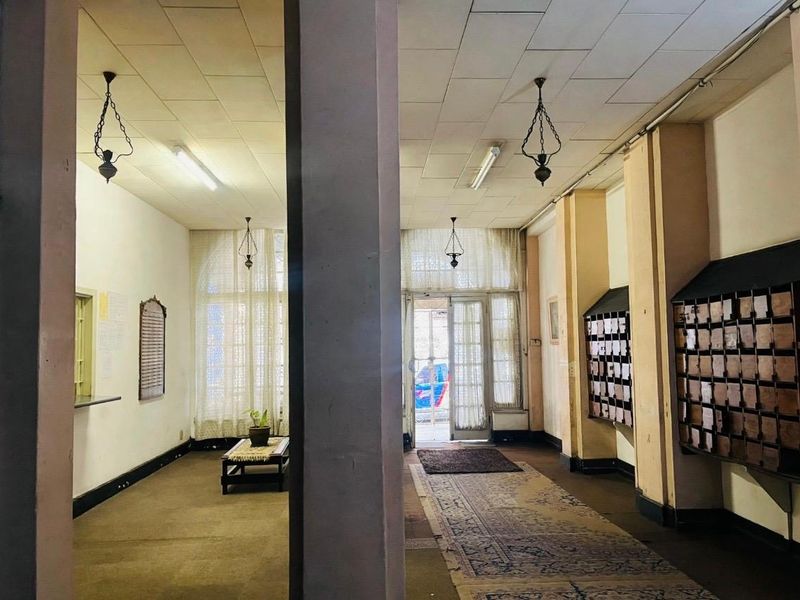 A dated apartment building entrance lobby featuring built-in mailboxes, tiled ceilings, and large glass doors leading to the exterior.