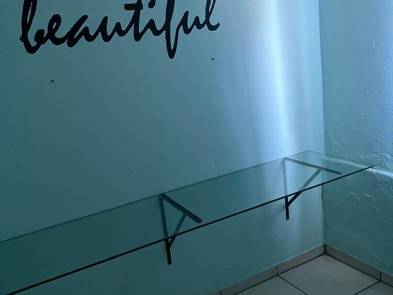 A small interior space featuring light blue walls, tiled flooring, and a wall-mounted glass shelf, suitable for a study or utility area.
