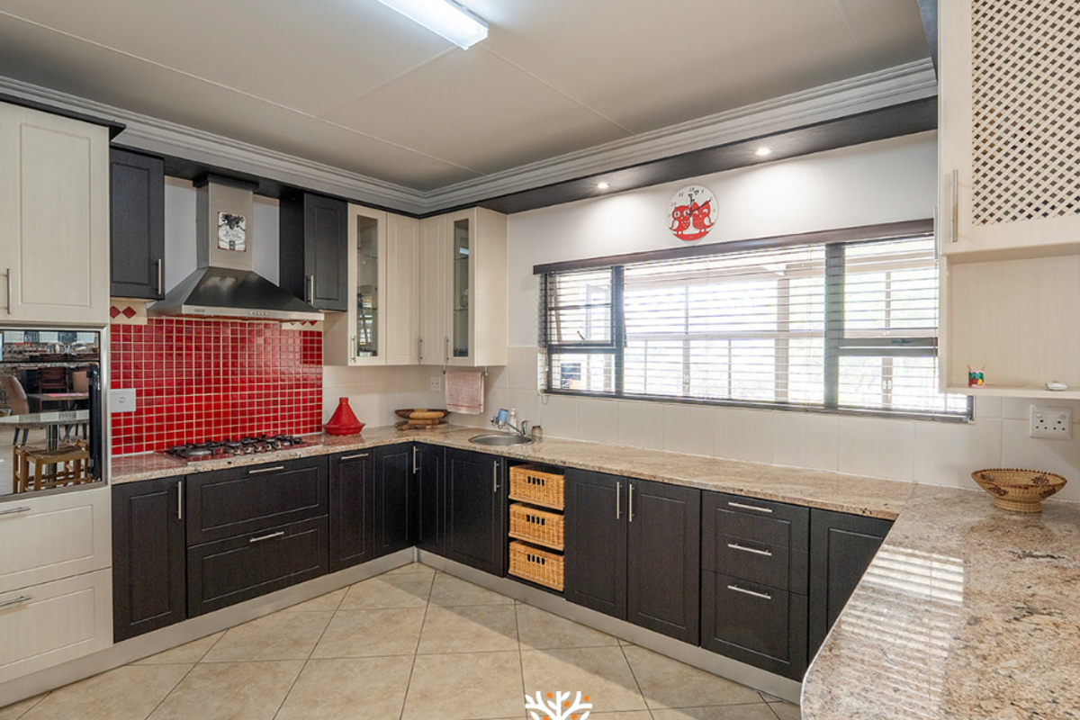 A functional kitchen featuring dark and light cabinetry, granite countertops, a red tiled splashback, built-in hob, extractor fan, and tiled flooring.