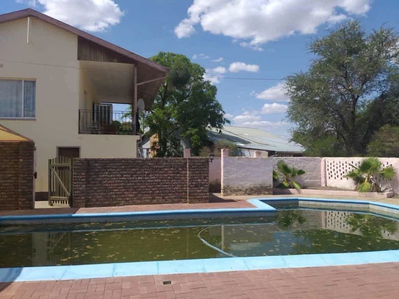 Outdoor pool area featuring a paved deck, brick boundary walls, and a balcony overlooking the swimming pool.