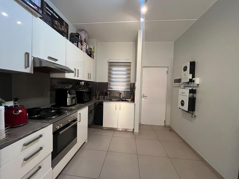 Modern kitchen featuring white gloss cabinetry, integrated appliances, tiled flooring, and a wall-mounted solar power inverter and battery system.
