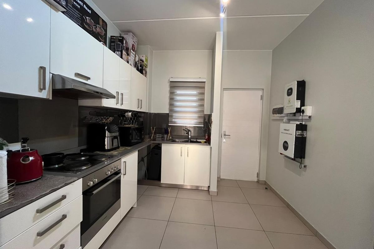 Modern kitchen featuring white gloss cabinetry, integrated appliances, tiled flooring, and a wall-mounted solar power inverter and battery system.