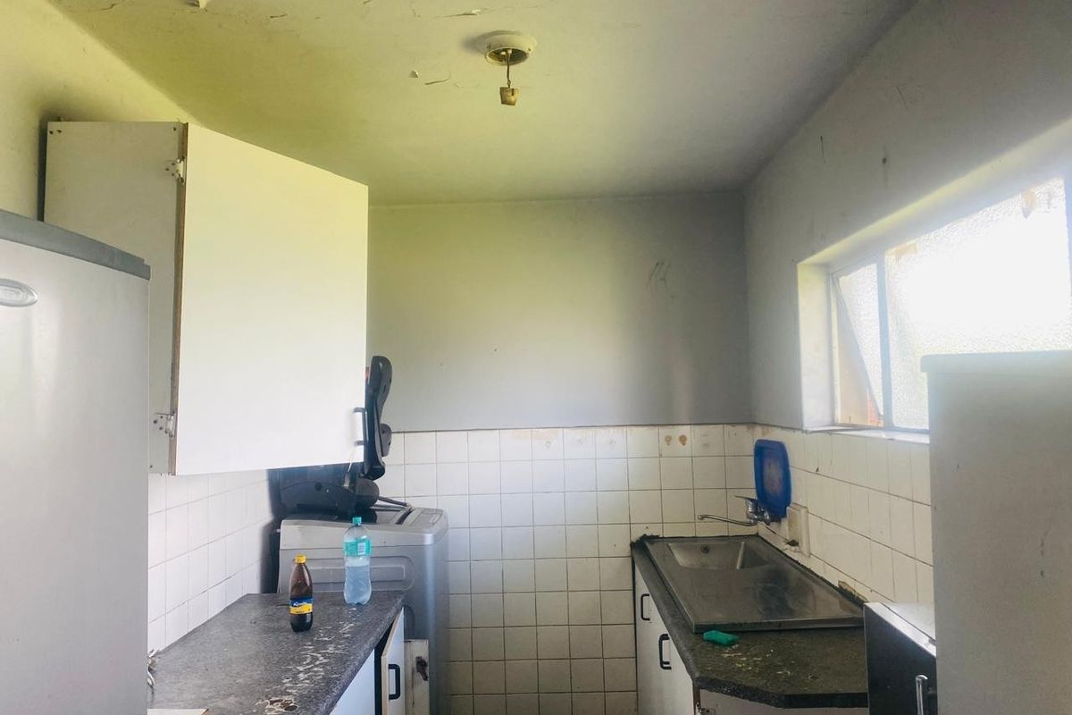 A dated kitchen area featuring tiled splashbacks, laminate countertops, and a stainless steel sink, currently requiring significant renovation and cosmetic repairs.