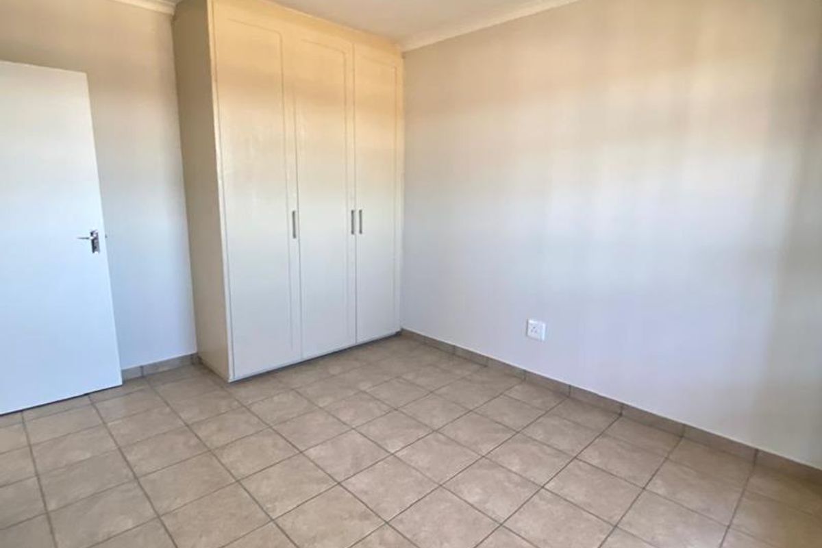 A clean, empty bedroom featuring neutral tiled flooring and a built-in wardrobe, offering a blank canvas for personalization.