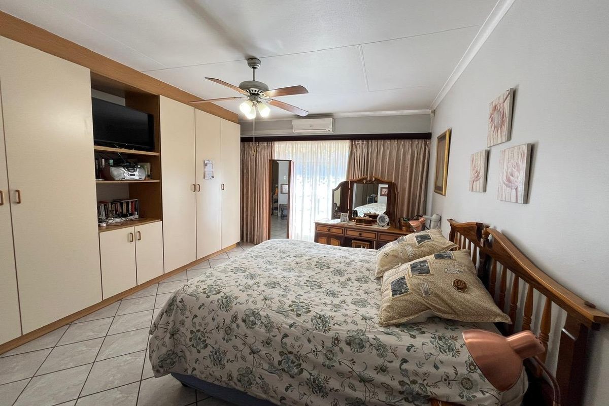 Spacious bedroom featuring extensive built-in cabinetry, tiled flooring, a ceiling fan, and a wall-mounted air conditioning unit.