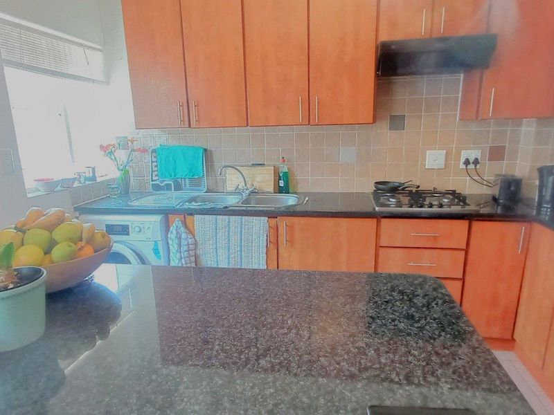 Functional kitchen featuring granite countertops, wooden cabinetry, gas hob, and integrated sink area with tiled backsplash.