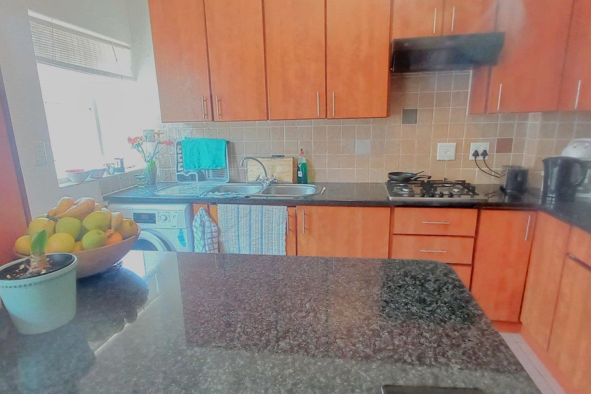 Functional kitchen featuring granite countertops, wooden cabinetry, gas hob, and integrated sink area with tiled backsplash.