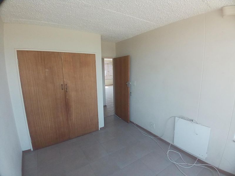 An empty bedroom featuring tiled flooring, a built-in wooden wardrobe, and a textured ceiling, offering a blank canvas for renovation.