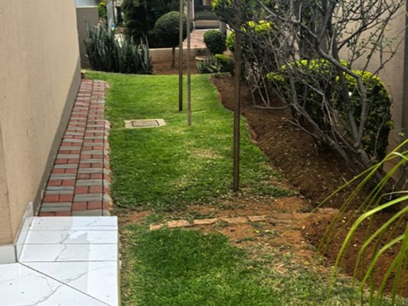A side garden area featuring a paved walkway, lawn, and boundary wall, providing a functional outdoor space along the side of the house.