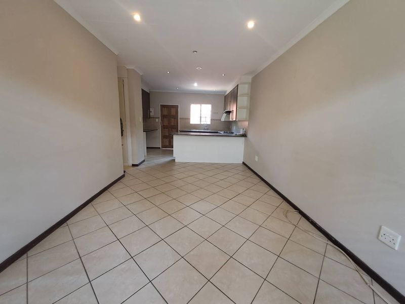 An open-plan living and kitchen area featuring tiled flooring, built-in cabinetry, and a breakfast counter, offering a blank canvas for interior design.